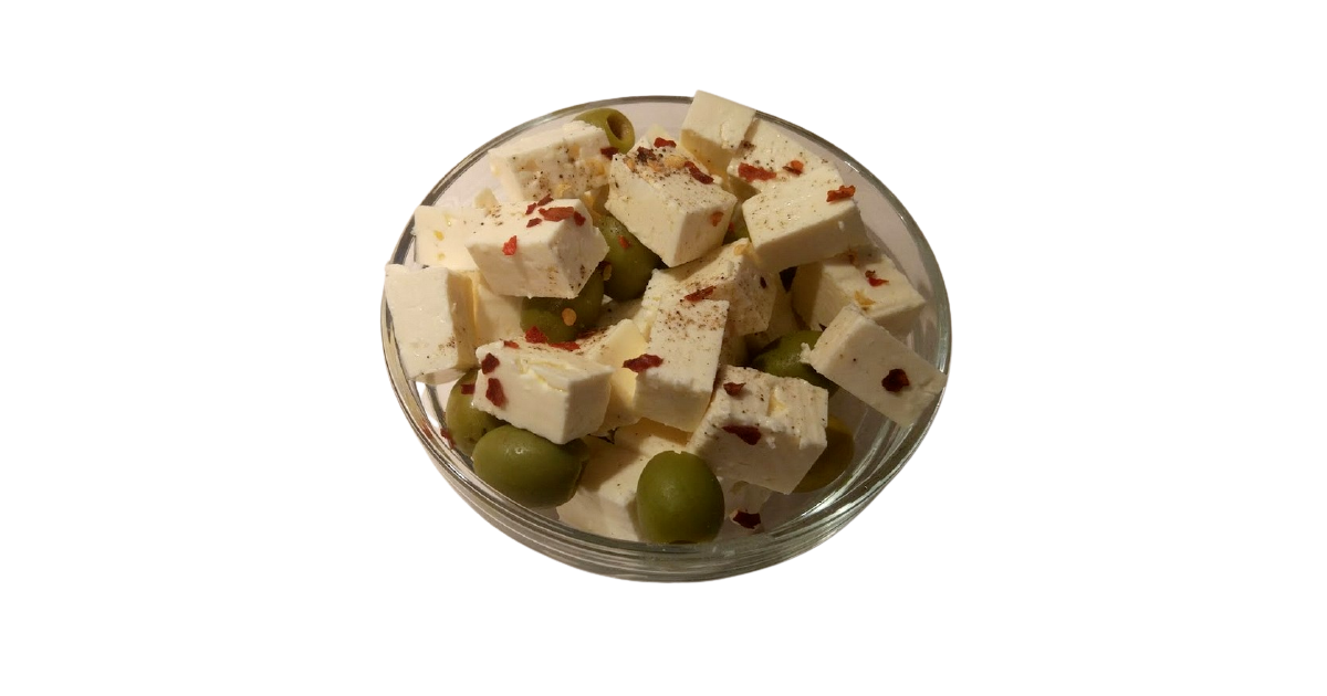 A small glass bowl filled with with pieces of white brined cheese and olives, sprinkled with chili flakes and ground black pepper.